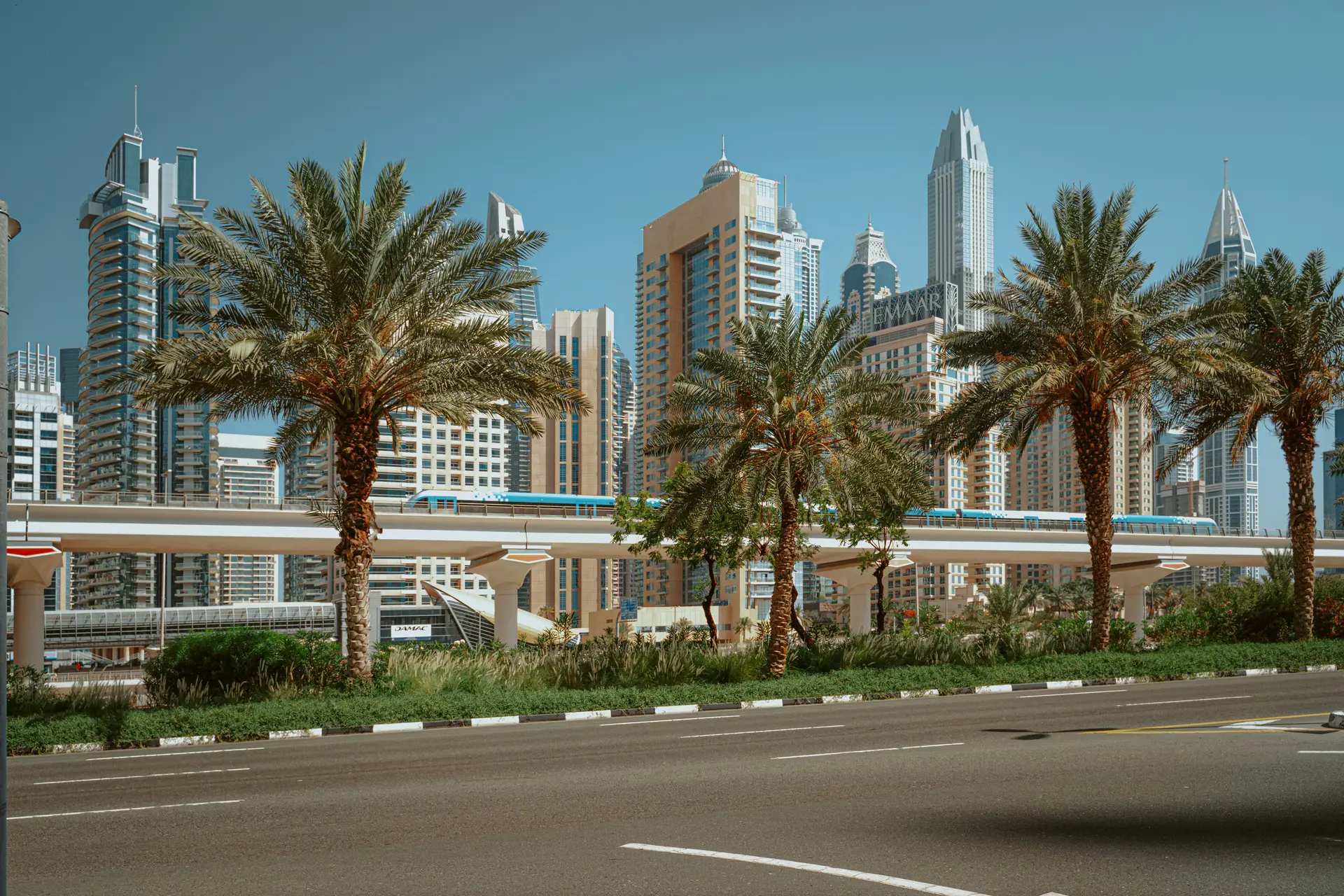 Sheikh Zayed Road in daylight, towers and palms either side of the elevated metro line.