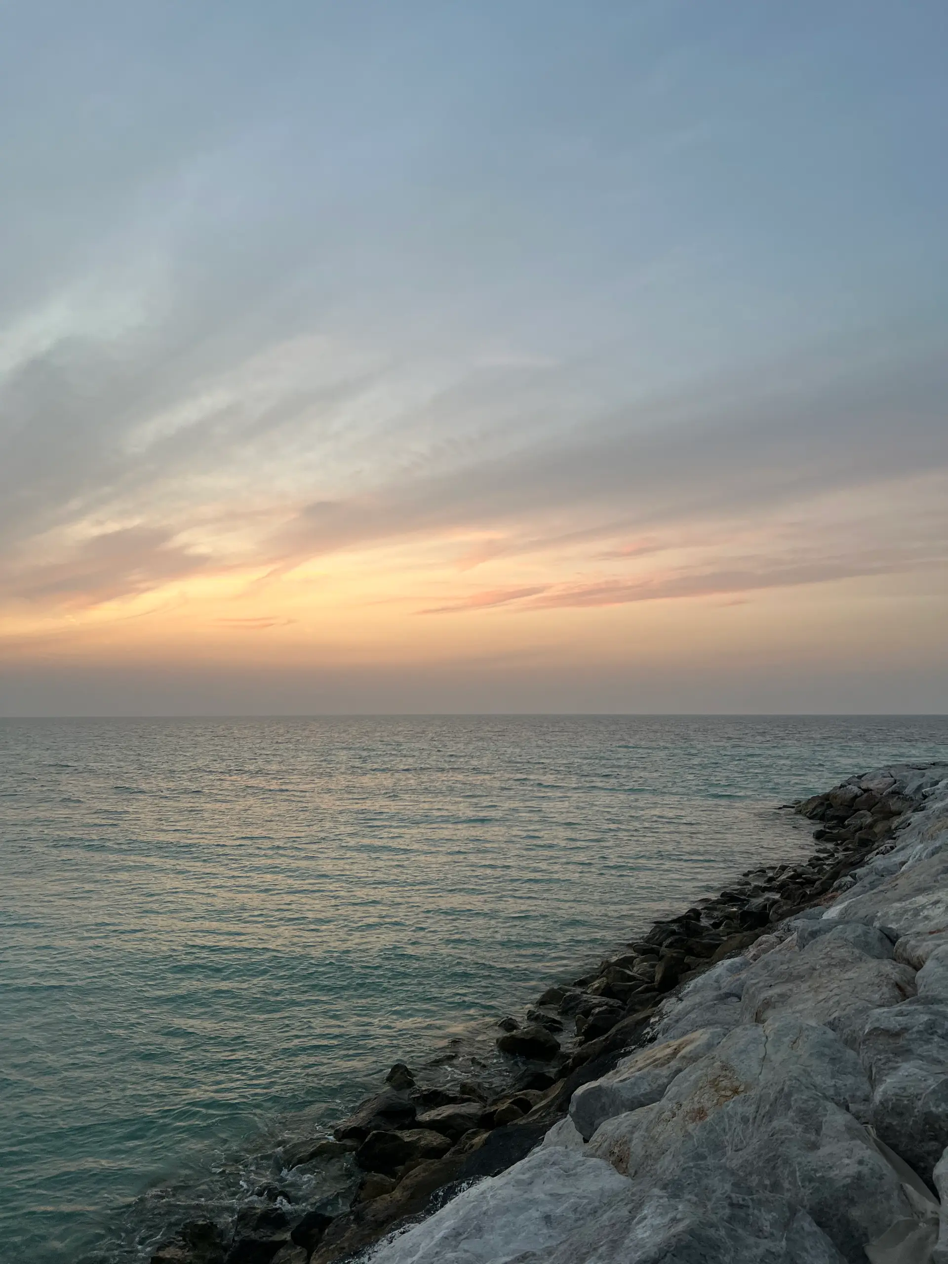 The shoreline at Umm Al Quwain at sunset, rock and shallow water against the Gulf.